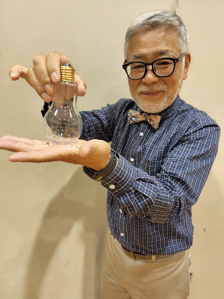 「シルク　イン　バルブ」というマジックです。 ひげ親父はシルクを左手で作った拳の中に入れていきます。 そして右手で電球を持ち振り上げて左手の拳に振り下ろすと左手に持っていたシルクが○○○の中から現れます！
